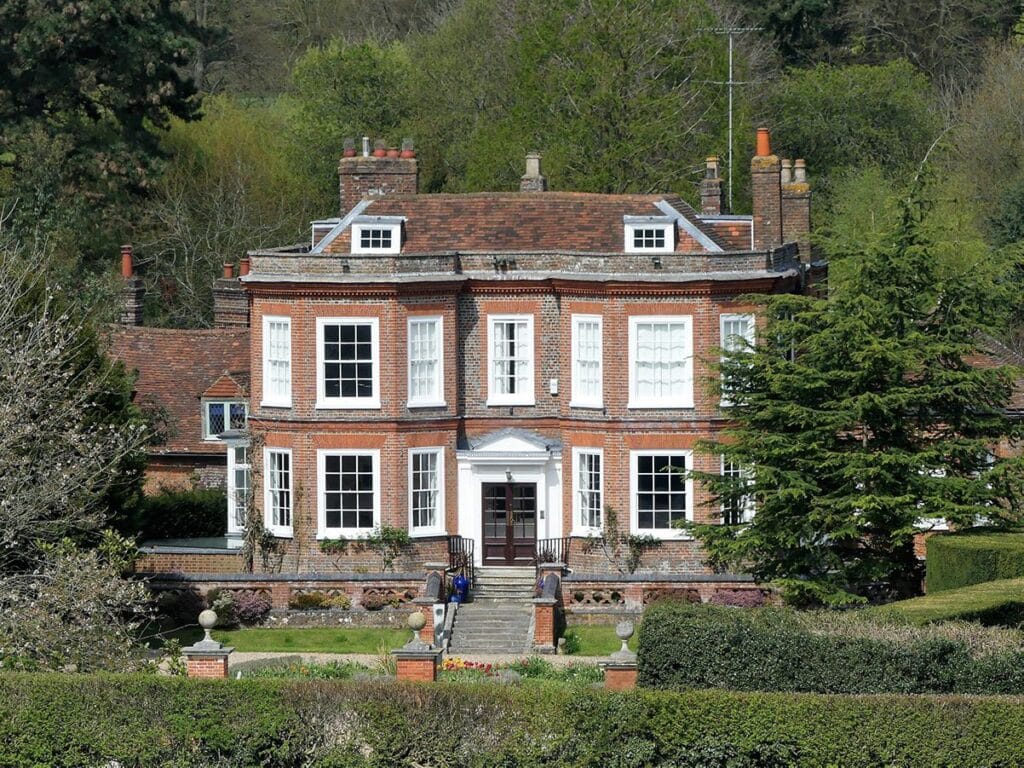 Grade II listed Georgian manor house with red brick facade, white sash windows, and symmetrical architecture set in landscaped gardens